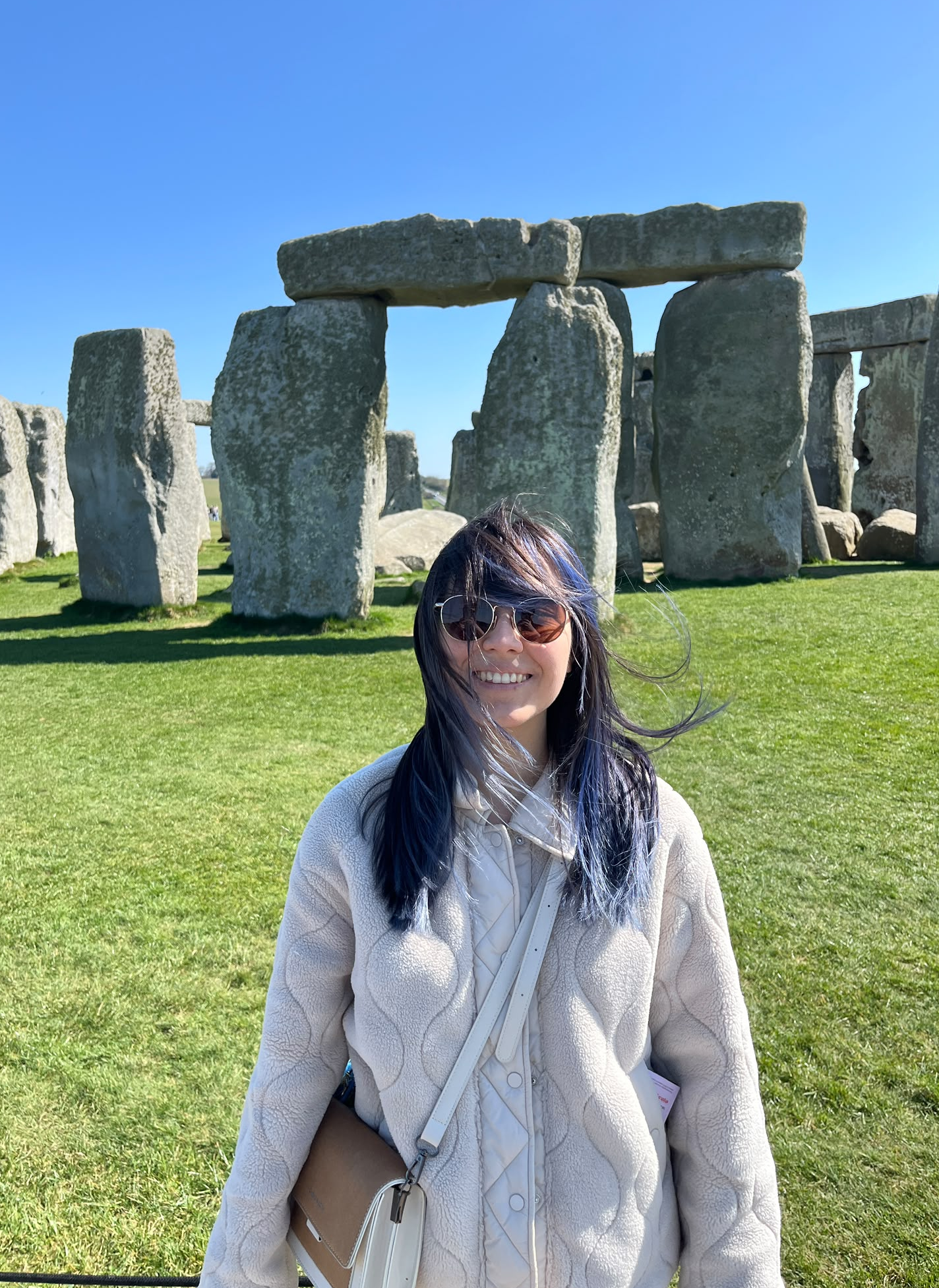 Arzu smiling in front of Stonehenge on a sunny day